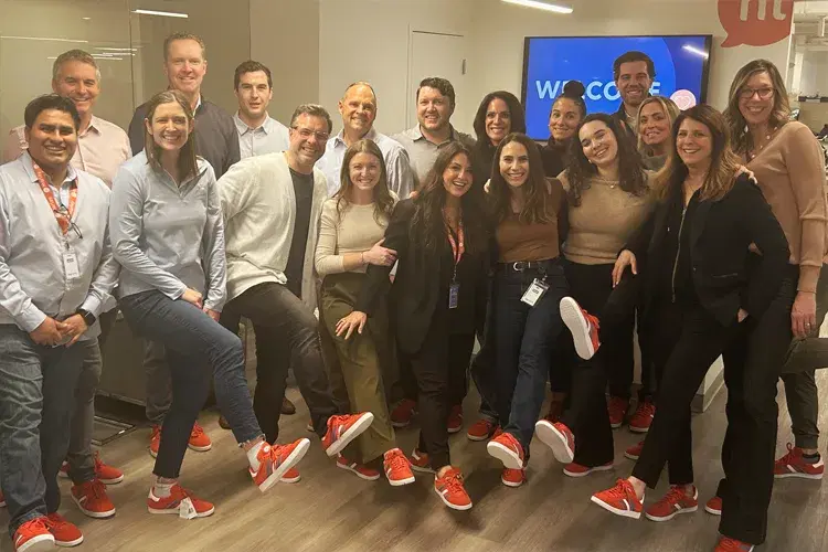Hi Marley team members gathered together in the office, many wearing matching red sneakers, in front of a welcome screen.